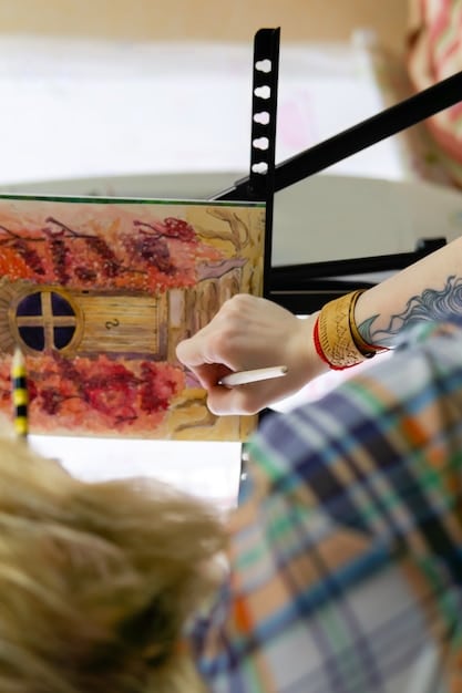 A close-up of an artist's hands meticulously painting details on a canvas at a local art fair, surrounded by other unique artworks.
