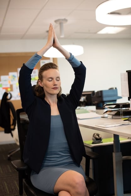 A person stretching their wrists and shoulders while sitting at a desk, with a blur of a modern, ergonomic office environment in the background. The focus is on gentle movement and relaxation.
