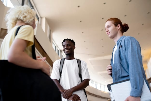 A diverse group of college students and professionals are engaged in a lively networking event in a modern, brightly lit university hall, shaking hands and exchanging business cards.