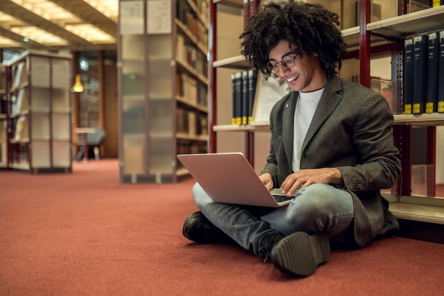 A student sitting in a modern university library abroad, surrounded by books, using a laptop, and looking intently at the screen, indicating academic focus and dedication.